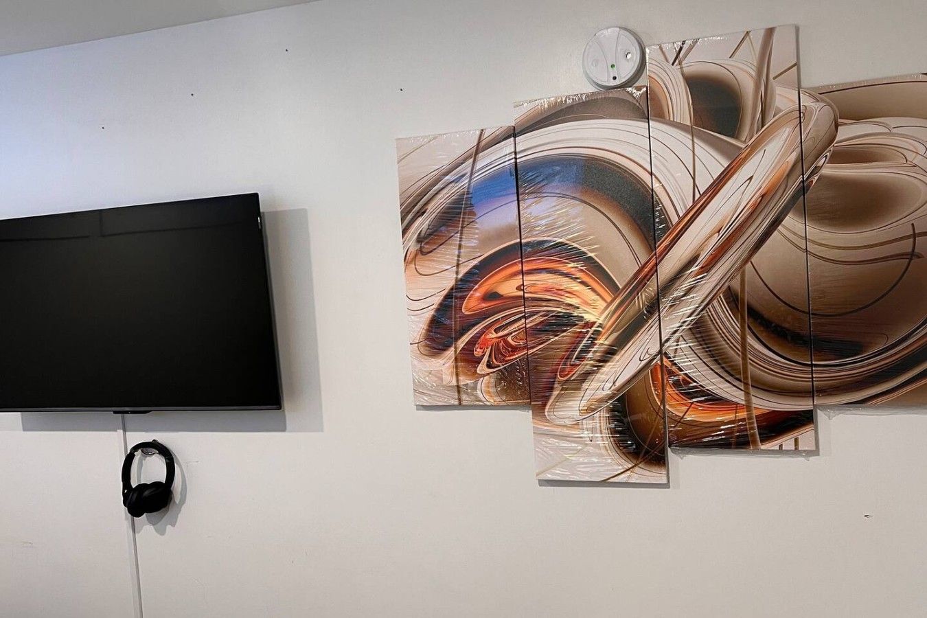 Televisão de tela plana na parede, com um grande quadro abstrato à direita.