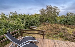 A wooden deck with a bench and a picnic table, surrounded by dense vegetation and trees. - 2 bedroom awesome home in Glesborg (Glesborg)