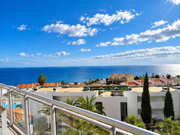 Área residencial costeira com vista clara para o mar, edifícios modernos e varanda com guarda-corpo de vidro.