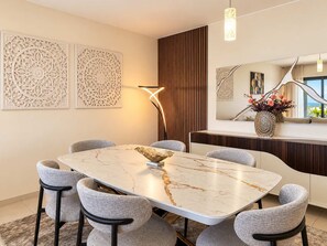 Uma área de refeições moderna com mesa de mármore, cadeiras estofadas cinzentas, painéis decorativos na parede e um abajur contemporâneo.