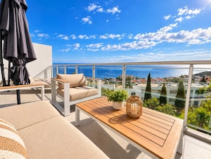 A balcony with a sofa, a wooden table, and a potted plant. - Sea View Apartment w/ Pool & Parking in Canico (Caniço)
