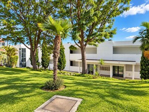 Un edifici modern de dues plantes amb una zona exterior coberta, envoltat de gespa ben cuidada i arbres.