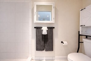 Une salle de bain comprenant des toilettes, un porte-serviettes avec deux serviettes, un porte-rouleau de papier toilette et une fenêtre au-dessus du lavabo.
