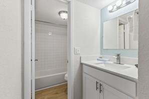Ein Badezimmer mit weißem Waschtisch, einem beleuchteten Spiegel, einer Badewanne und einer Dusche.