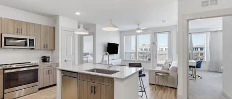 Una cocina moderna con una isla central, horno empotrado, microondas y comedor con vista a la ciudad.