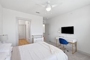 Un dormitorio con cama, escritorio, silla, televisor y ventilador de techo.