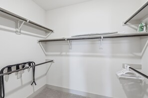 Ein weißer Schrank mit Kleiderstangen, einer kleinen Ablage mit einer grünen Flasche und einem Gestell mit gefalteter Kleidung.