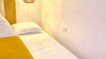 A single bed with a white mattress and a yellow blanket, a wooden headboard, and a hanging light fixture.