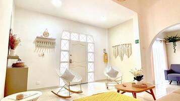 Habitación de hotel moderna con una cama, dos sillones mecedores, una mesita y un detalle decorativo en la pared.