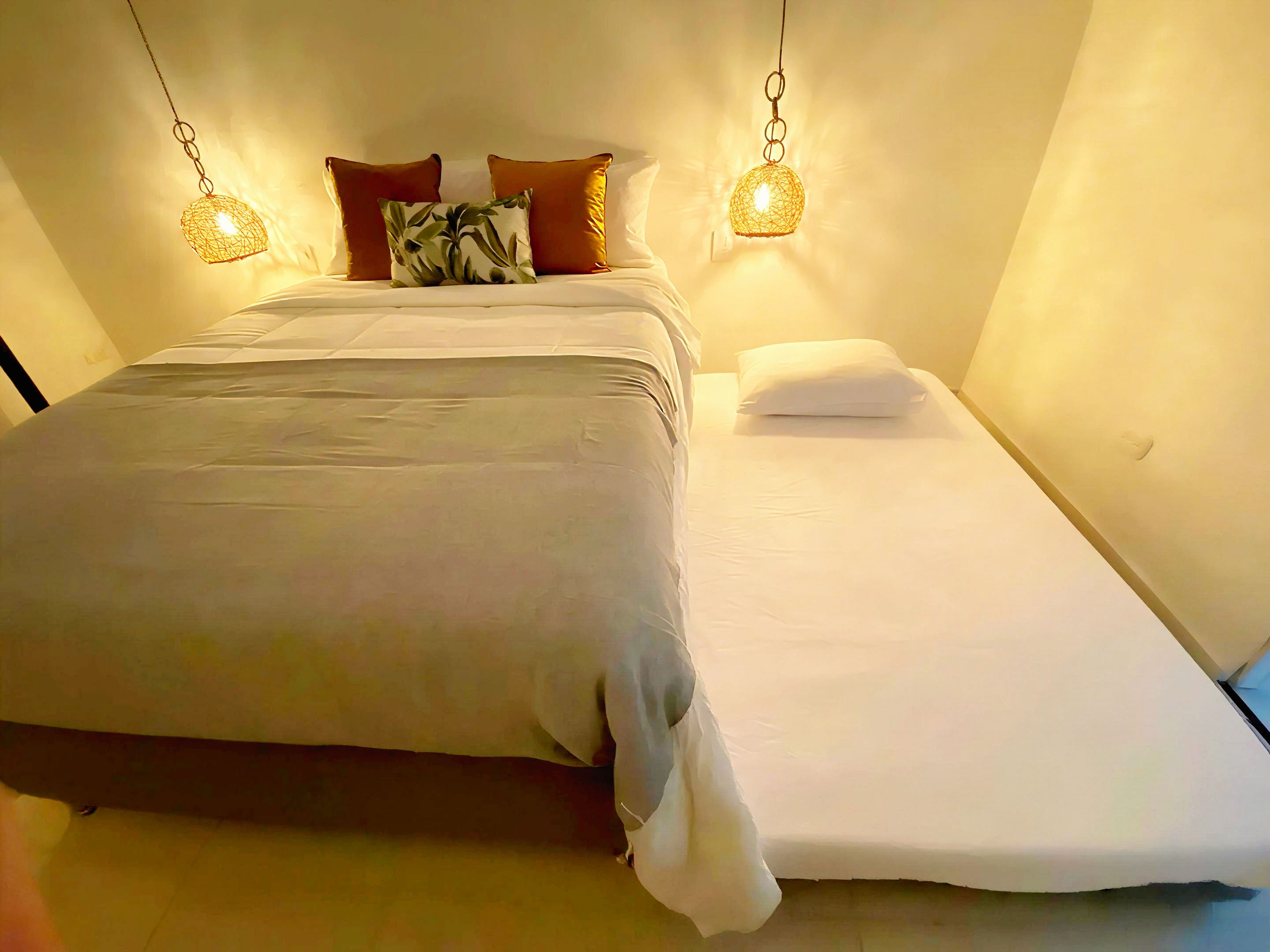 Un lit avec une couverture grise, des oreillers blancs et un luminaire suspendu au-dessus.
