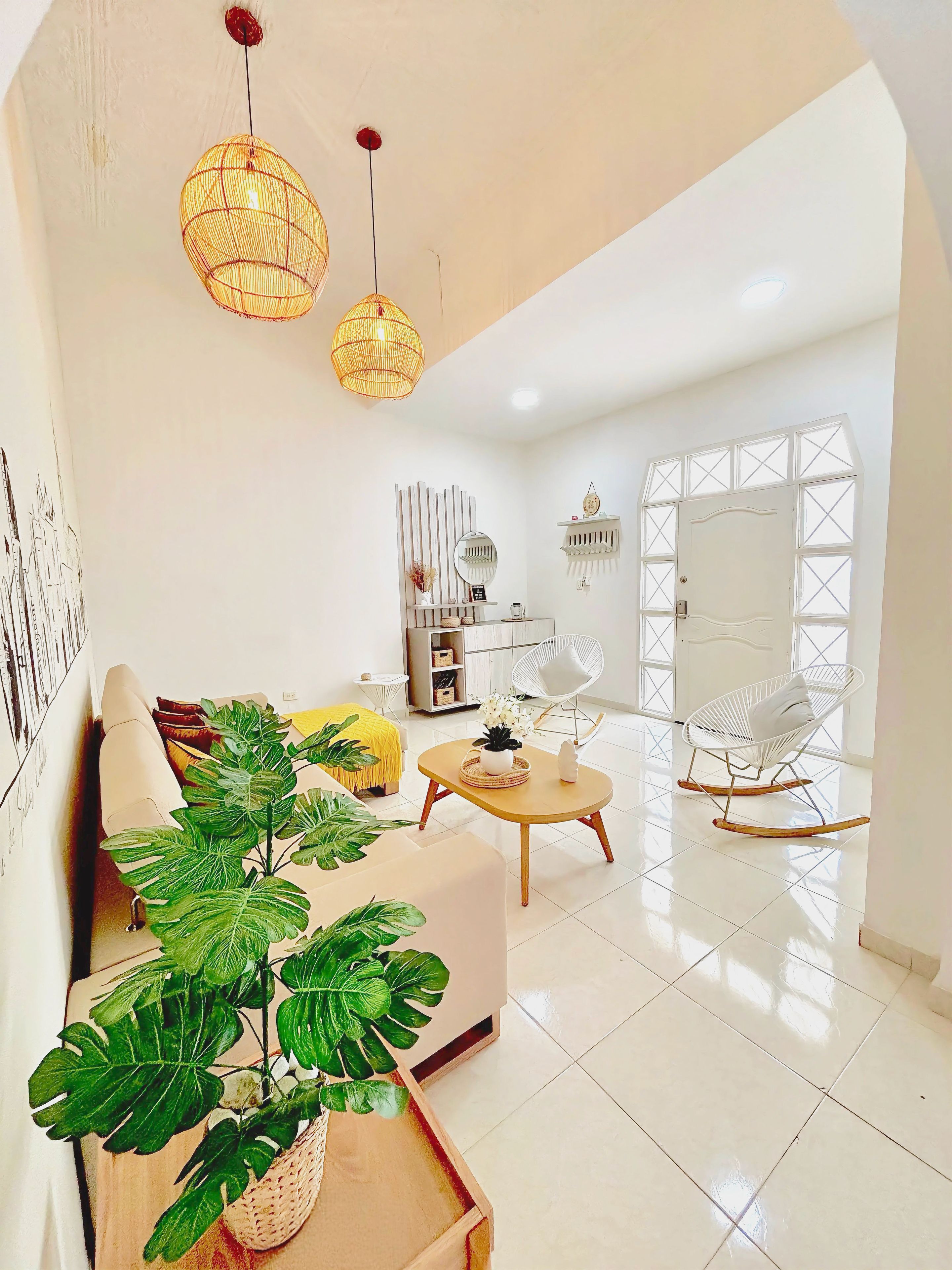 A modern living room with a sofa, coffee table, and a large plant. There are two hanging lights and a white door with a window.