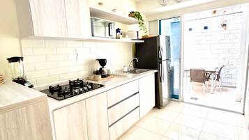 A modern kitchen with white cabinetry, a black stove, and a refrigerator. There are clocks on the wall and a plant on the counter.
