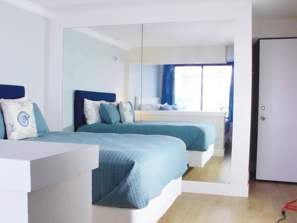 Un dormitorio con dos camas, un espejo grande y vistas a un balcón.