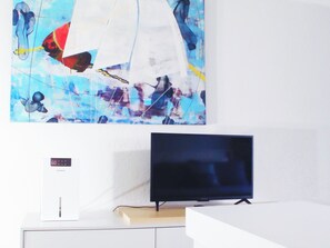 Ein Flachbildfernseher auf einem weißen Stand, eine weiße Unterhaltungseinheit mit einer digitalen Uhr und ein farbenfrohes abstraktes Gemälde an der Wand.