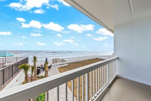 Ein Balkon mit Blick auf den Strand, eine Sitzgruppe mit Tisch und Stühlen sowie ein kleiner Garten mit Palmen.