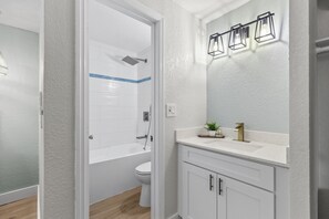 Ein Badezimmer mit einer weißen Badewanne, einer Toilette und einem Waschbecken mit Spiegel darüber.