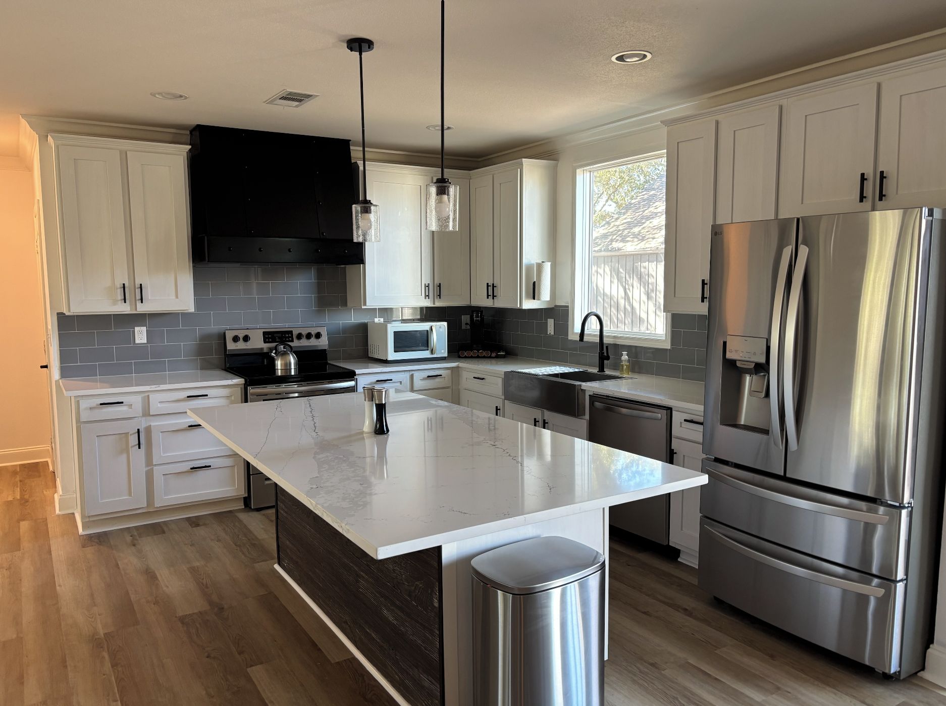 A modern kitchen with white cabinets, stainless steel appliances, and a marble island.
