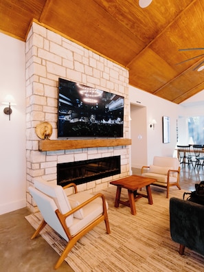 A modern living room with a fireplace, comfortable seating, and a large flat-screen TV mounted on a brick wall.