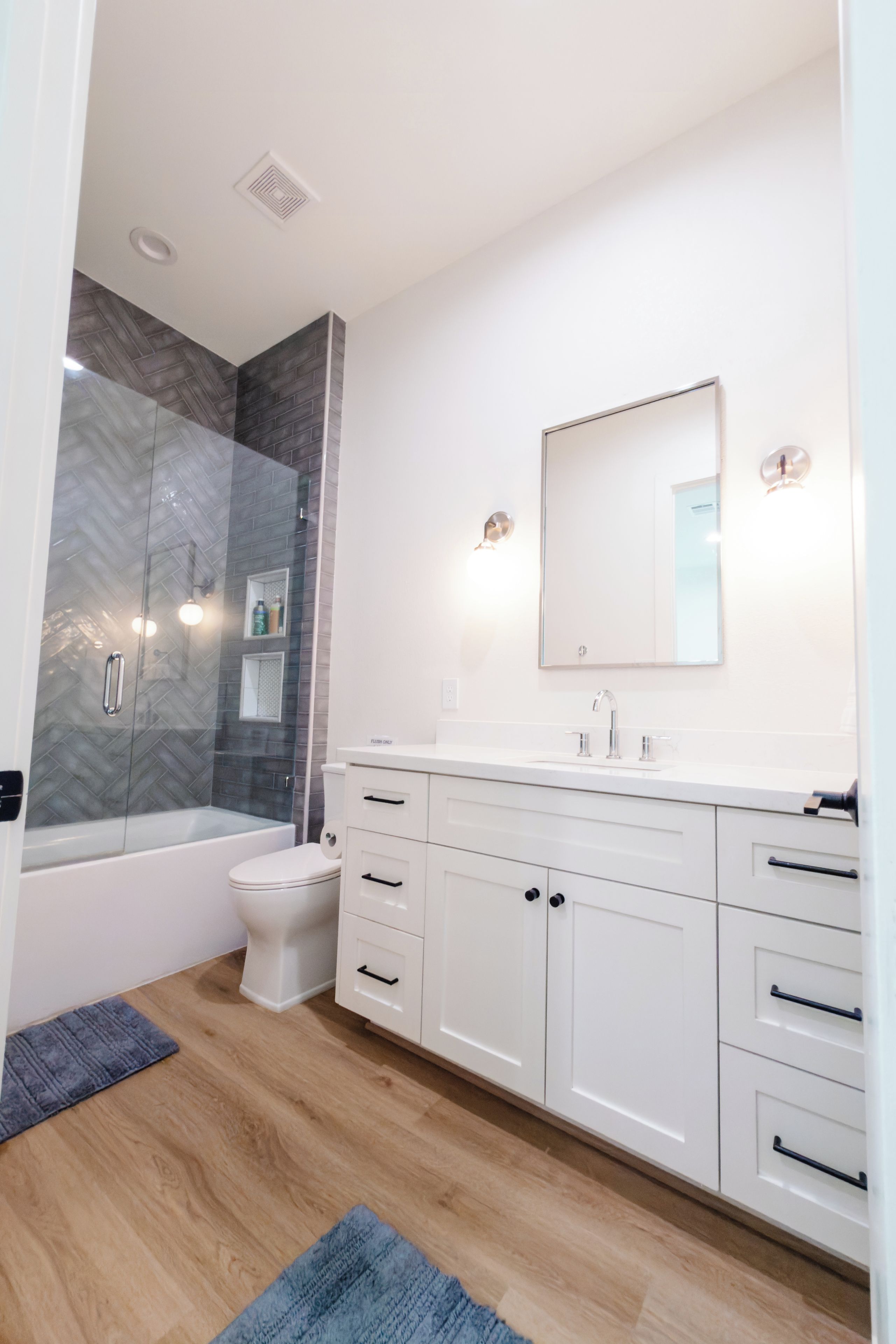 Un baño moderno con cabina de ducha de vidrio, inodoro blanco, tocador con espejo y suelo de madera.