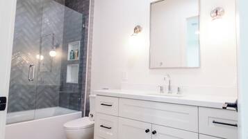 Un baño moderno con cabina de ducha de vidrio, inodoro blanco, tocador con espejo y suelo de madera.