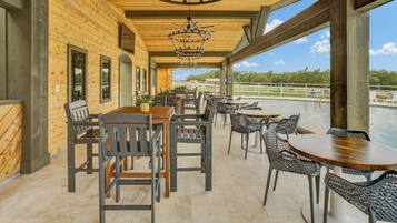 An outdoor dining area with wooden tables and chairs, a chandelier, and a view of a body of water.