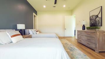 A bedroom with two beds, a ceiling fan, a nightstand with a lamp, a dresser, and a door leading to another room.