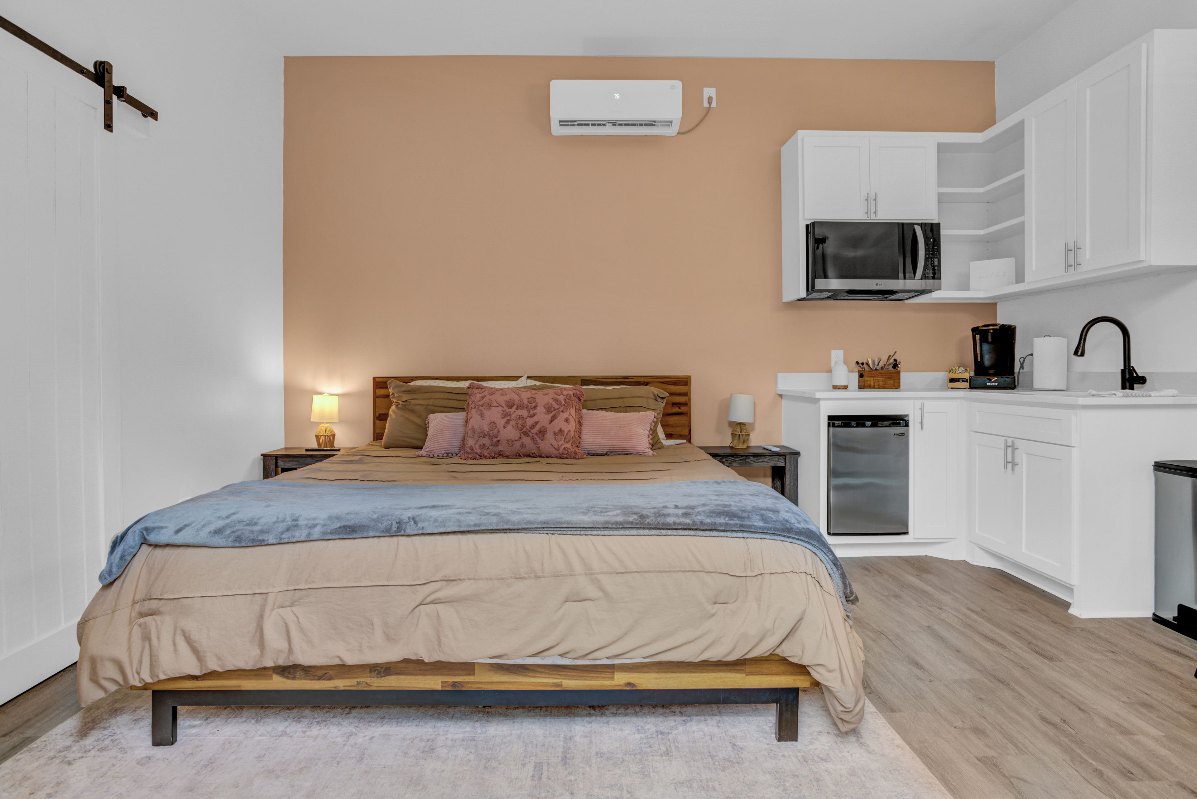 A bedroom with a bed, bedside tables, a lamp, a wardrobe, a microwave, and a refrigerator.