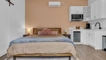 A bedroom with a bed, bedside tables, a lamp, a wardrobe, a microwave, and a refrigerator.