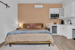A bedroom with a bed, bedside tables, a lamp, a wardrobe, a microwave, and a refrigerator.