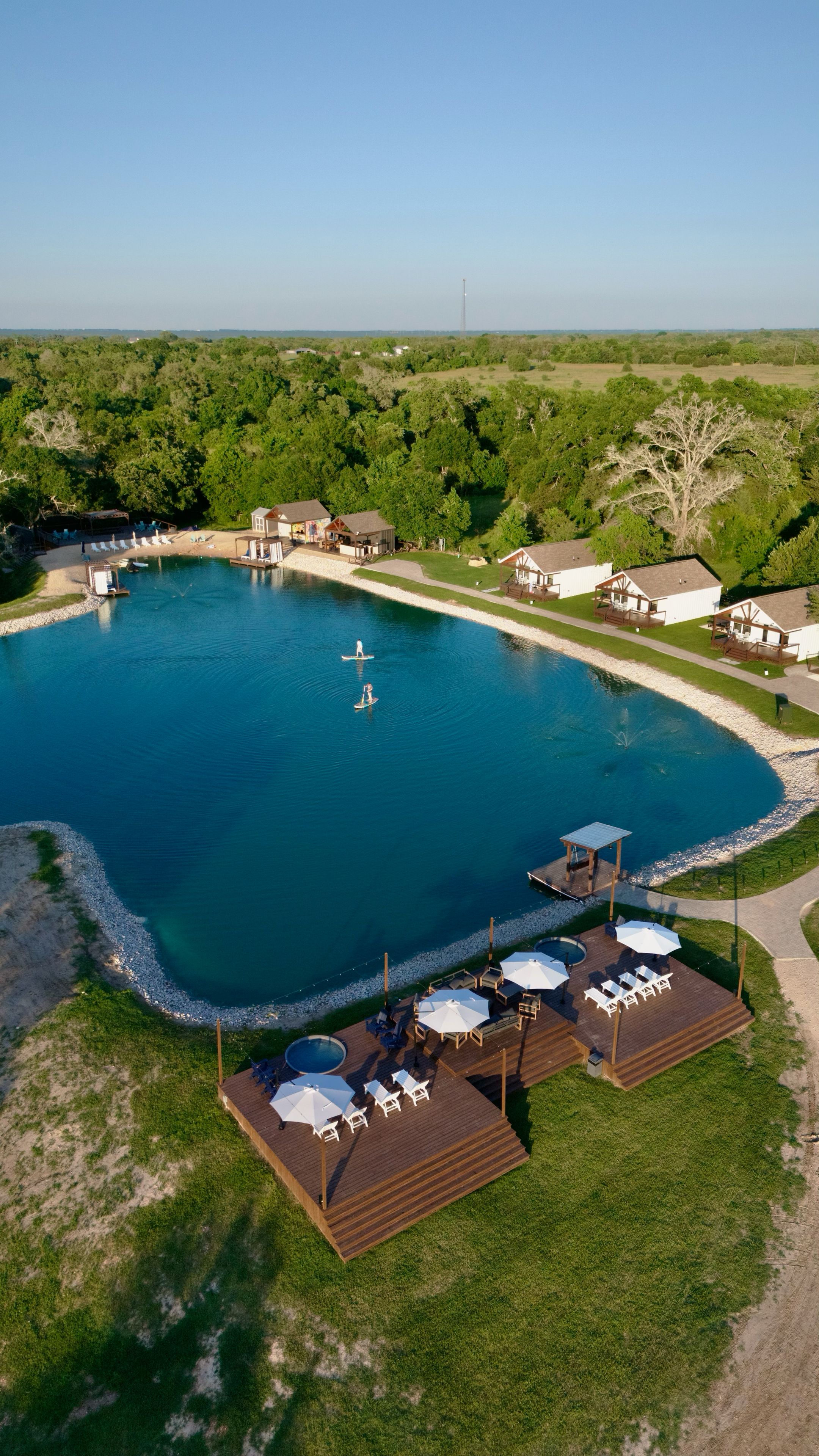 An aerial view of a resort with a large swimming pool, lounge areas, and a dock.