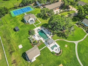 Vista aérea de una propiedad residencial con piscina, cancha de tenis y un pabellón.