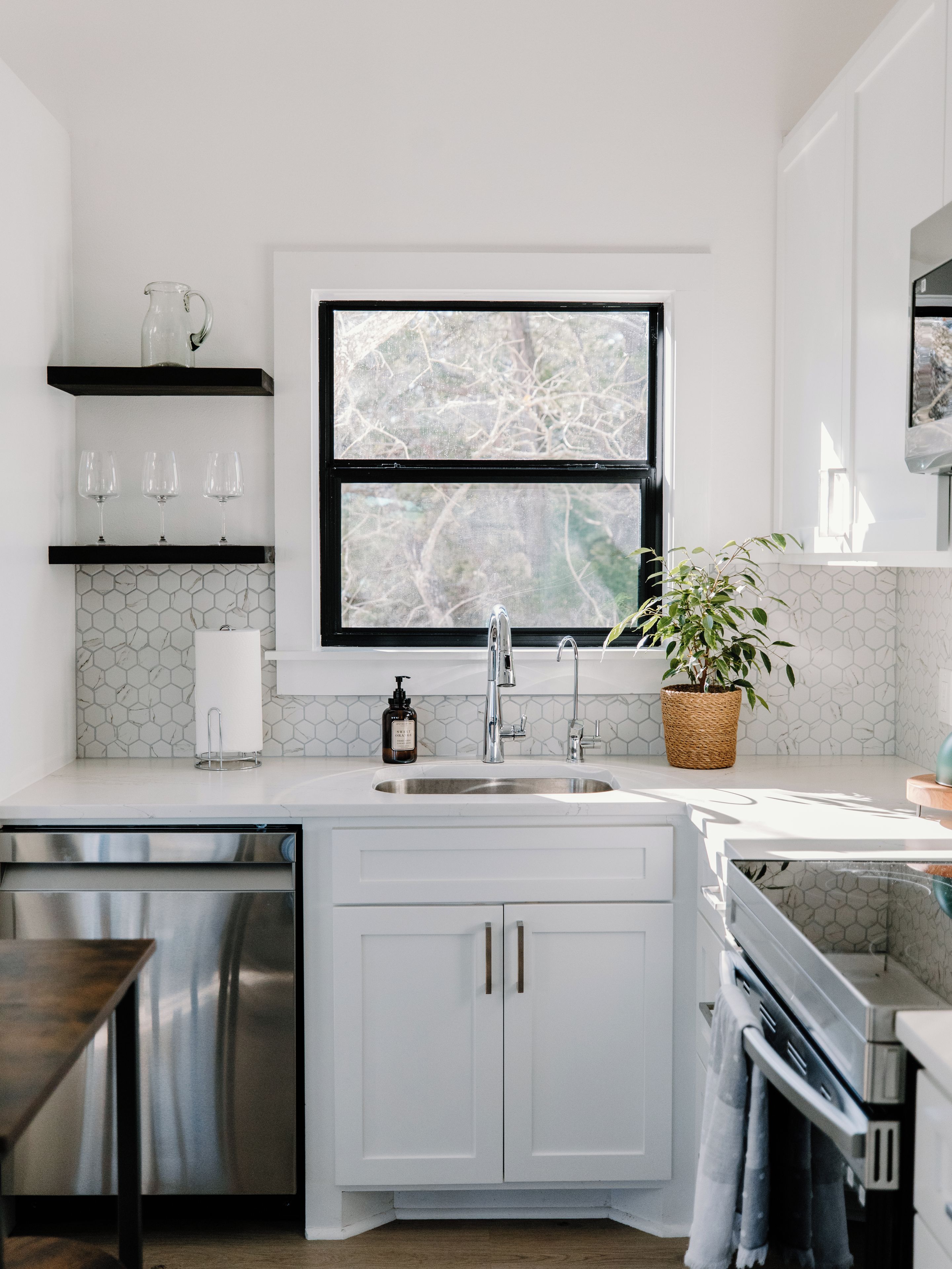 A modern kitchen with a double sink, stainless steel appliances, and a window with a view of trees.