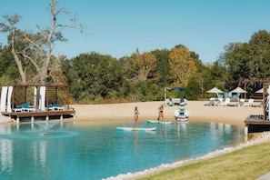 A pool area with lounge chairs, a wooden deck, and a sandy beach.