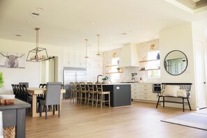 A modern kitchen with a central island, wooden chairs, and pendant lighting.
