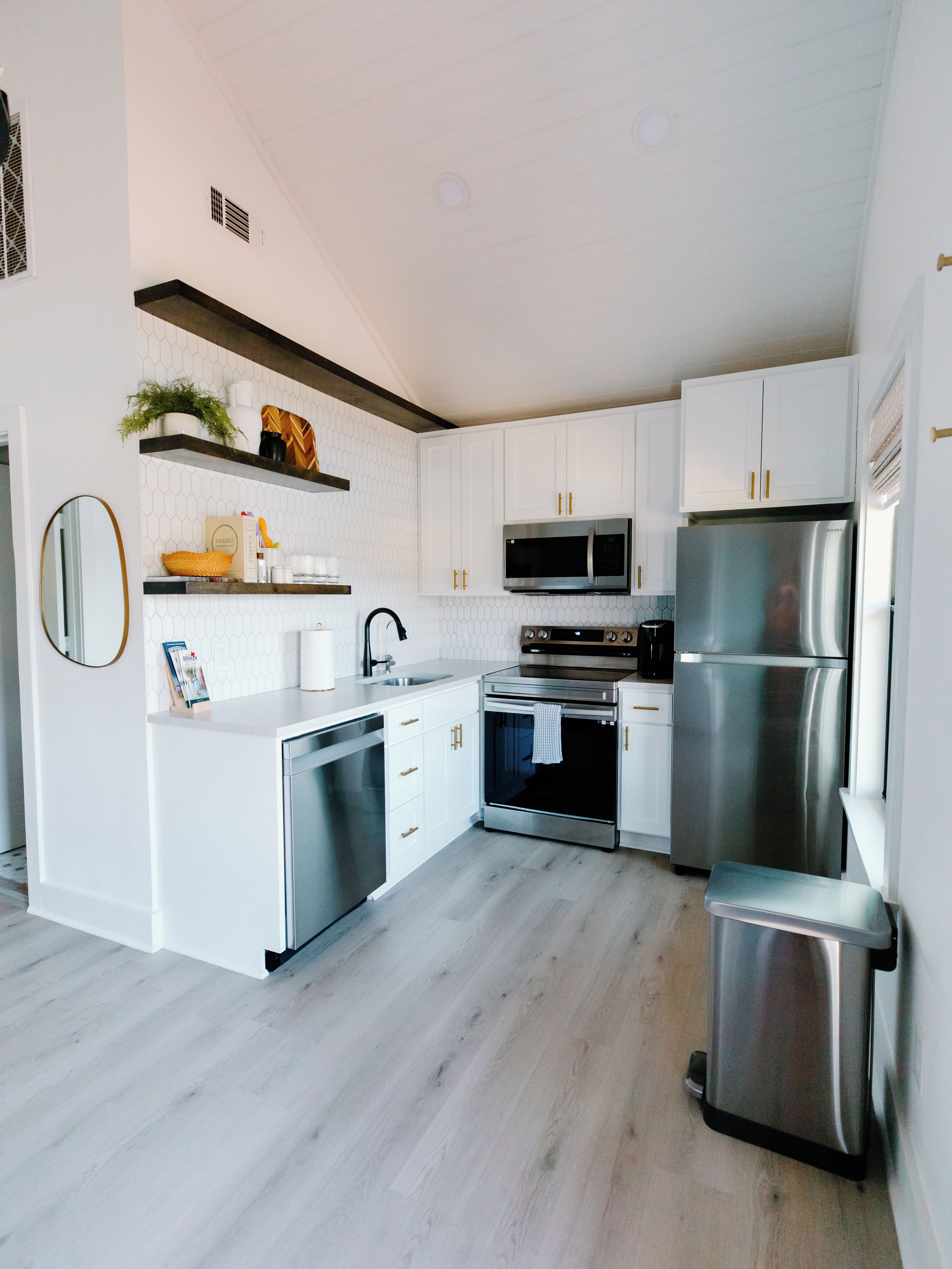 A modern kitchen with white cabinetry, stainless steel appliances, and a wooden floor.