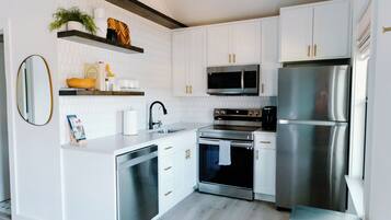 A modern kitchen with white cabinetry, stainless steel appliances, and a wooden floor.
