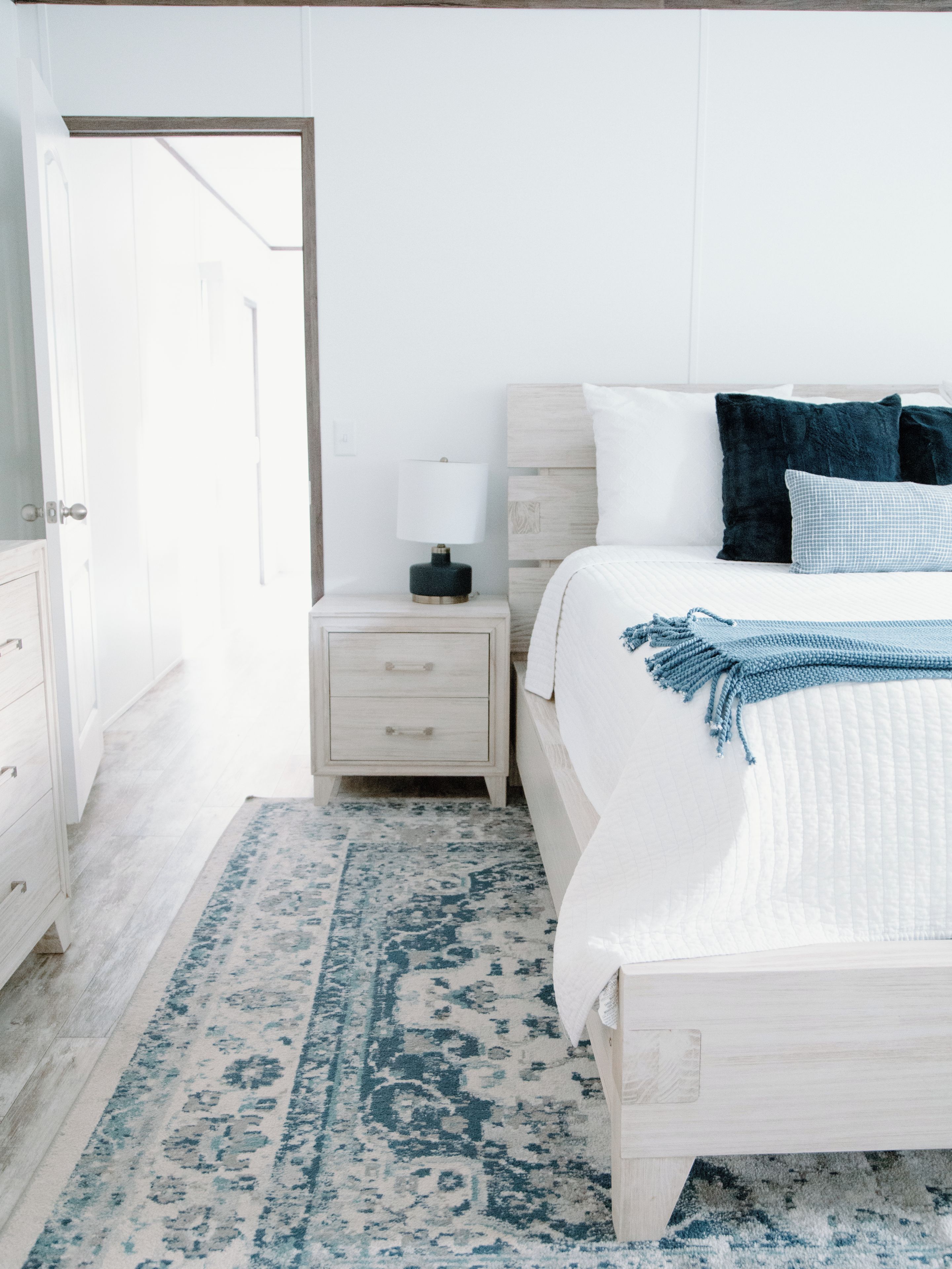 Un dormitorio con cama, mesita de noche, cómoda y una alfombra estampada.