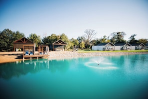 A lakeside property with a dock, lounge chairs, and a clear blue pool.