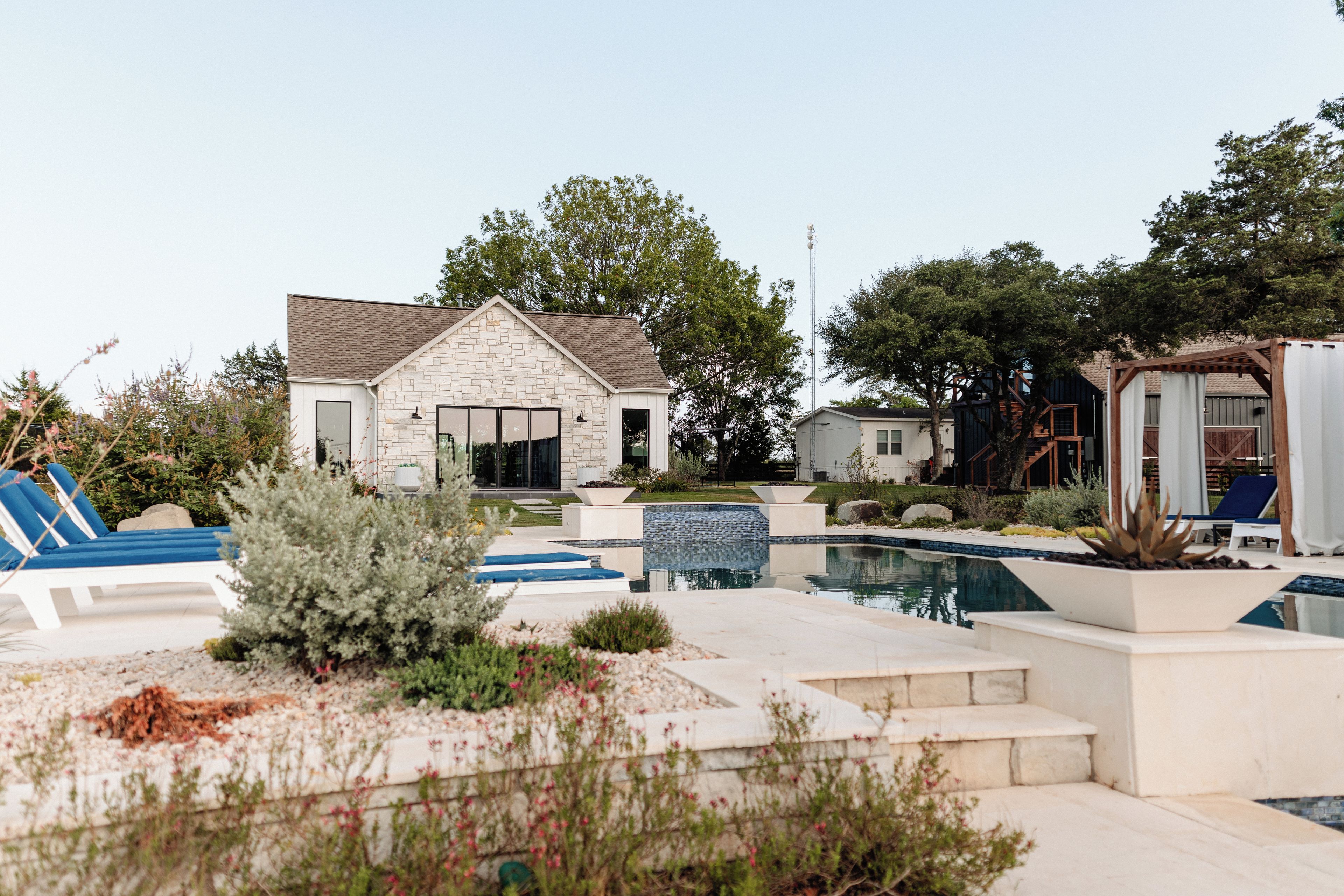 A modern house with a stone facade, a swimming pool, and a patio area with lounge chairs.