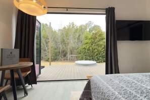 A hotel room with a bed, a table with a sign, and a view of the outdoors.