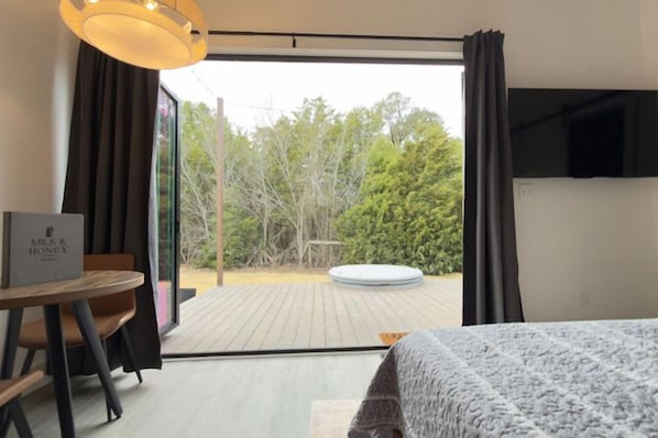 A hotel room with a bed, a table with a sign, and a view of the outdoors.