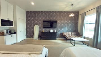 A hotel room with two beds, a television, a sofa, and a desk with a flat-screen TV.