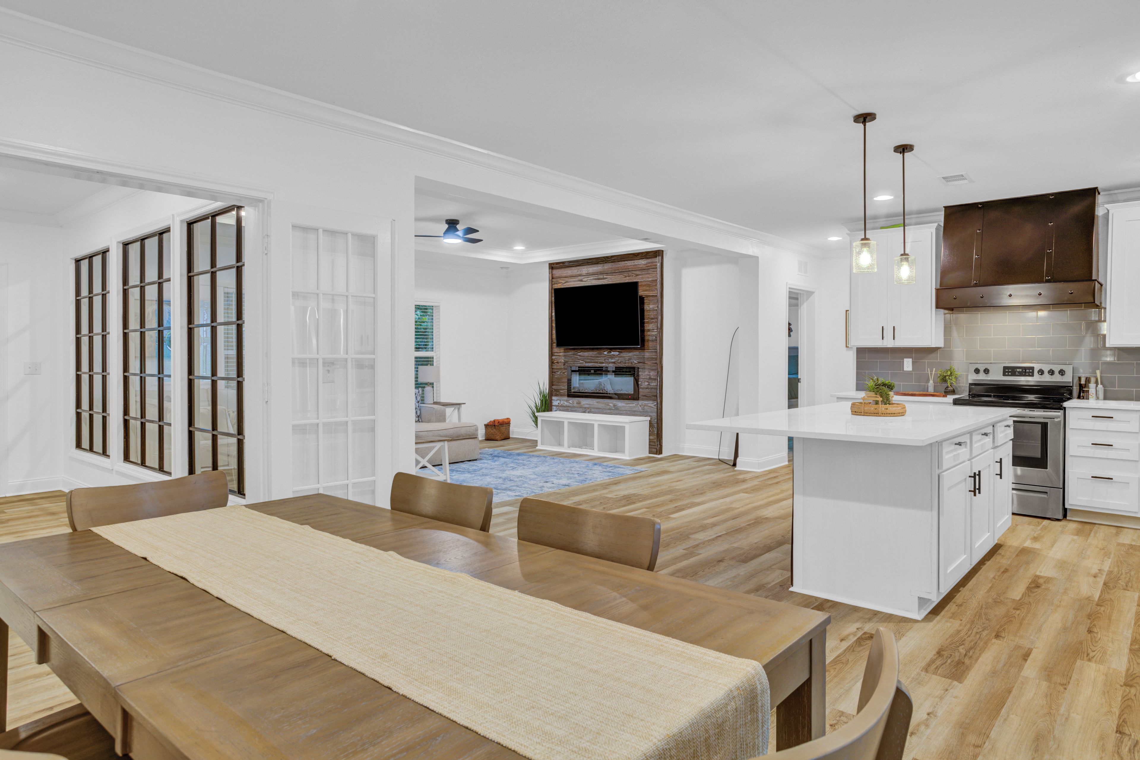 Una cocina moderna con armarios blancos, horno integrado y un comedor con mesa y sillas de madera.