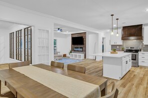 A modern kitchen with white cabinetry, a built-in oven, and a dining area with a wooden table and chairs.