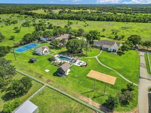 An aerial view of a residential area with a swimming pool, tennis court, and multiple houses.