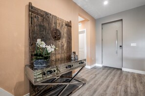 A hallway with a rustic wooden wall, a metal console table with a vase of white flowers, and a modern door. - Premium Family Townhouse Near Disney & Orlando Attractions (Kissimmee)