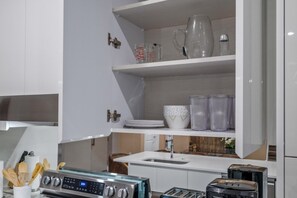 A modern kitchen with white cabinetry, a stainless steel range hood, a built-in oven, a sink, and a countertop with a toaster and a kettle. - Upscale Vacation Home Near Disney Parks (Kissimmee)