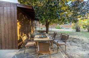 Eine Außenpatio mit Tisch und Stühlen, einer Holzpergola und einem Baum, der Schatten spendet.