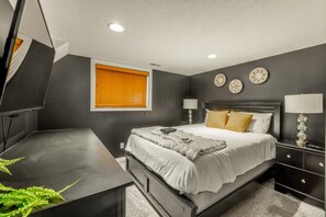 Ein Schlafzimmer mit einem Bett, Nachttischen, einem Schreibtisch und einem Fenster mit Jalousien.