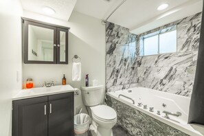 Ein modernes Badezimmer mit Marmorwand, einer Badewanne, einer Toilette und einem Waschtisch mit Spiegel.